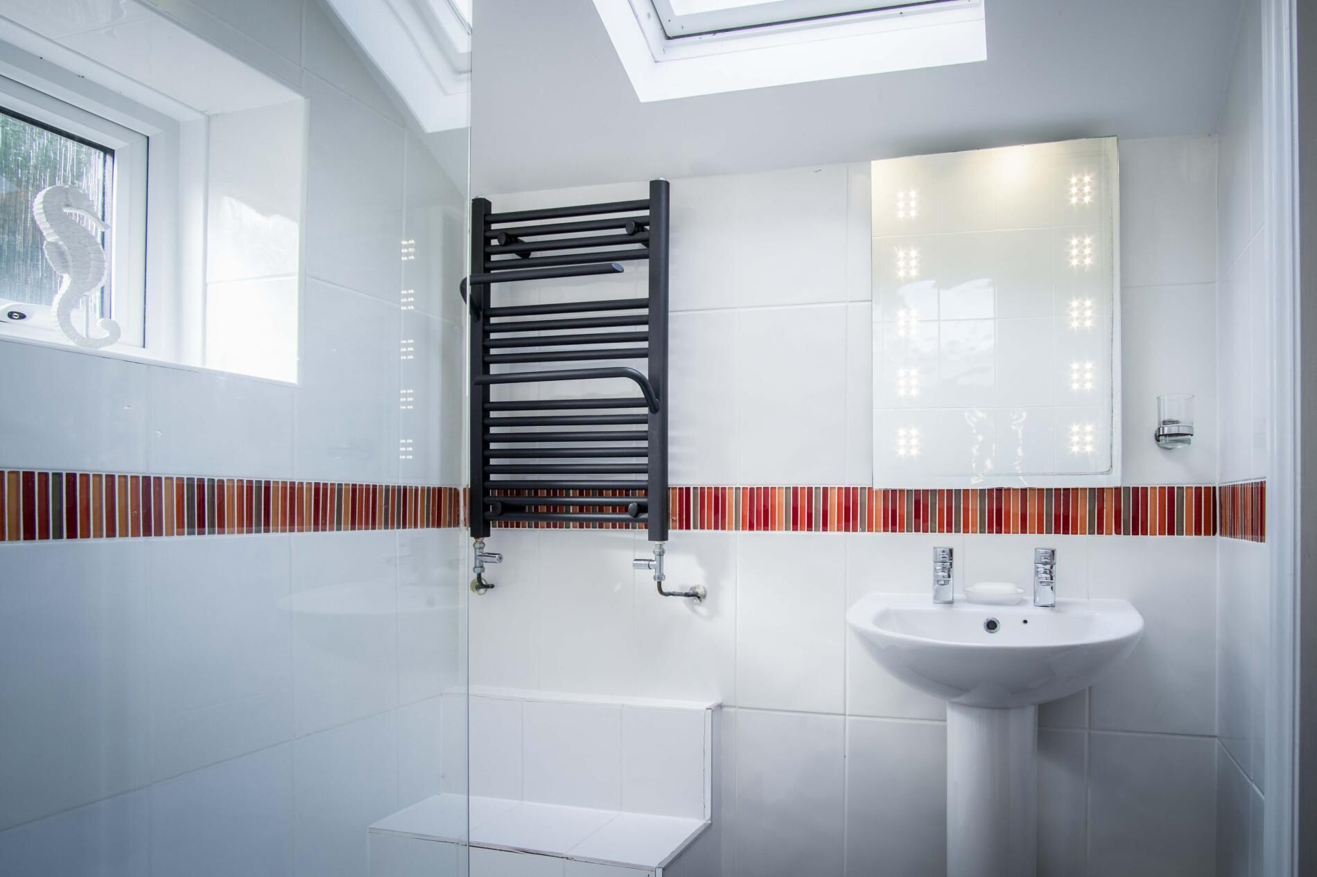 A modern bathroom with a skylight, a glass shower enclosure, a white sink, and a towel rack.
