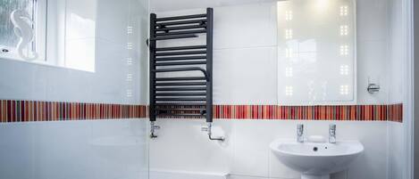 A modern bathroom with a skylight, a glass shower enclosure, a white sink, and a towel rack.