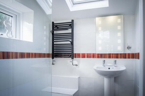 Een moderne badkamer met dakraam, een douchecabine van glas, een zwarte handdoekhouder, een witte wastafel en een betegelde spatwand.