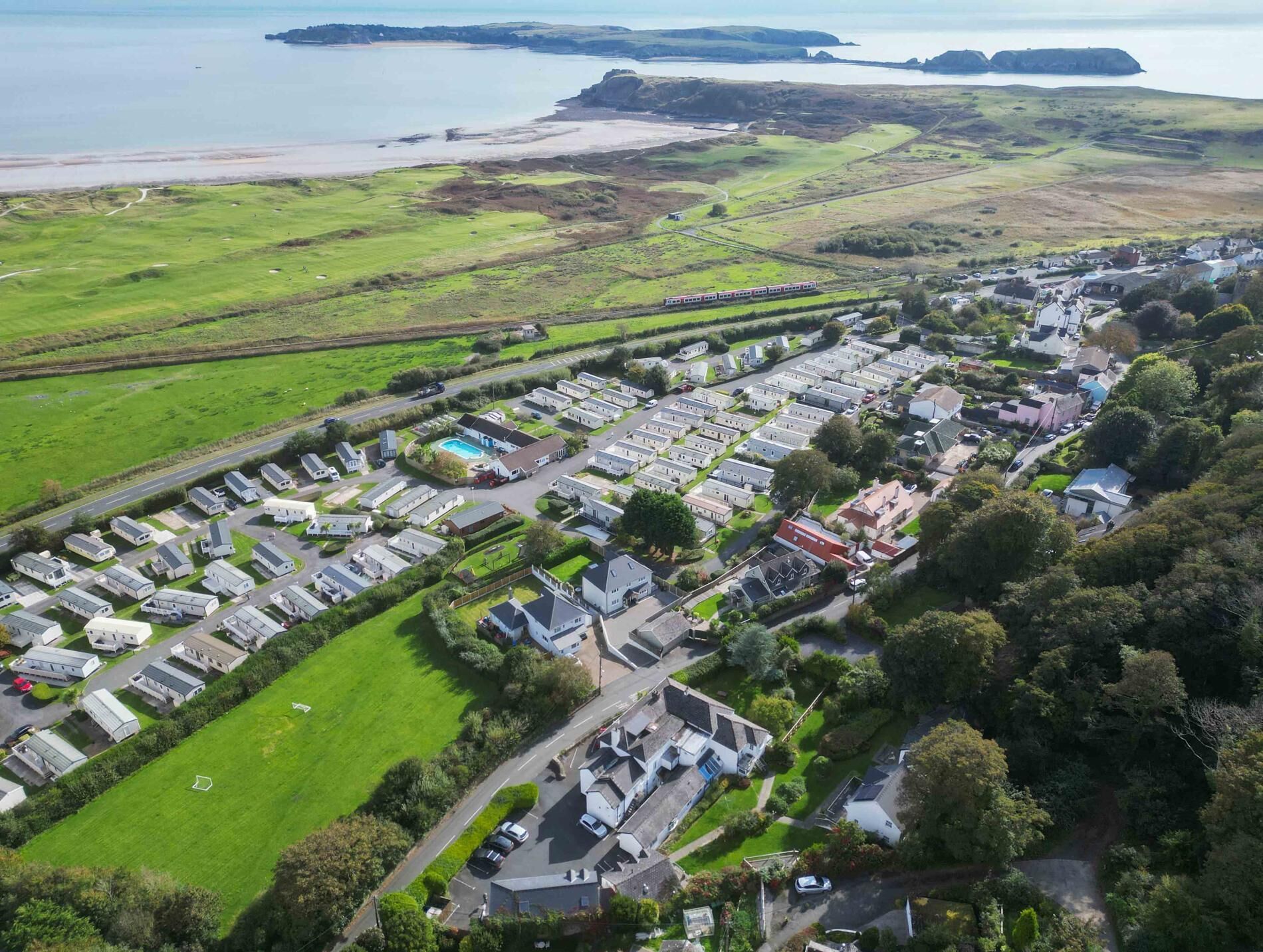 An aerial view of a caravan park with rows of caravans, a swimming pool, and a beach in the background.