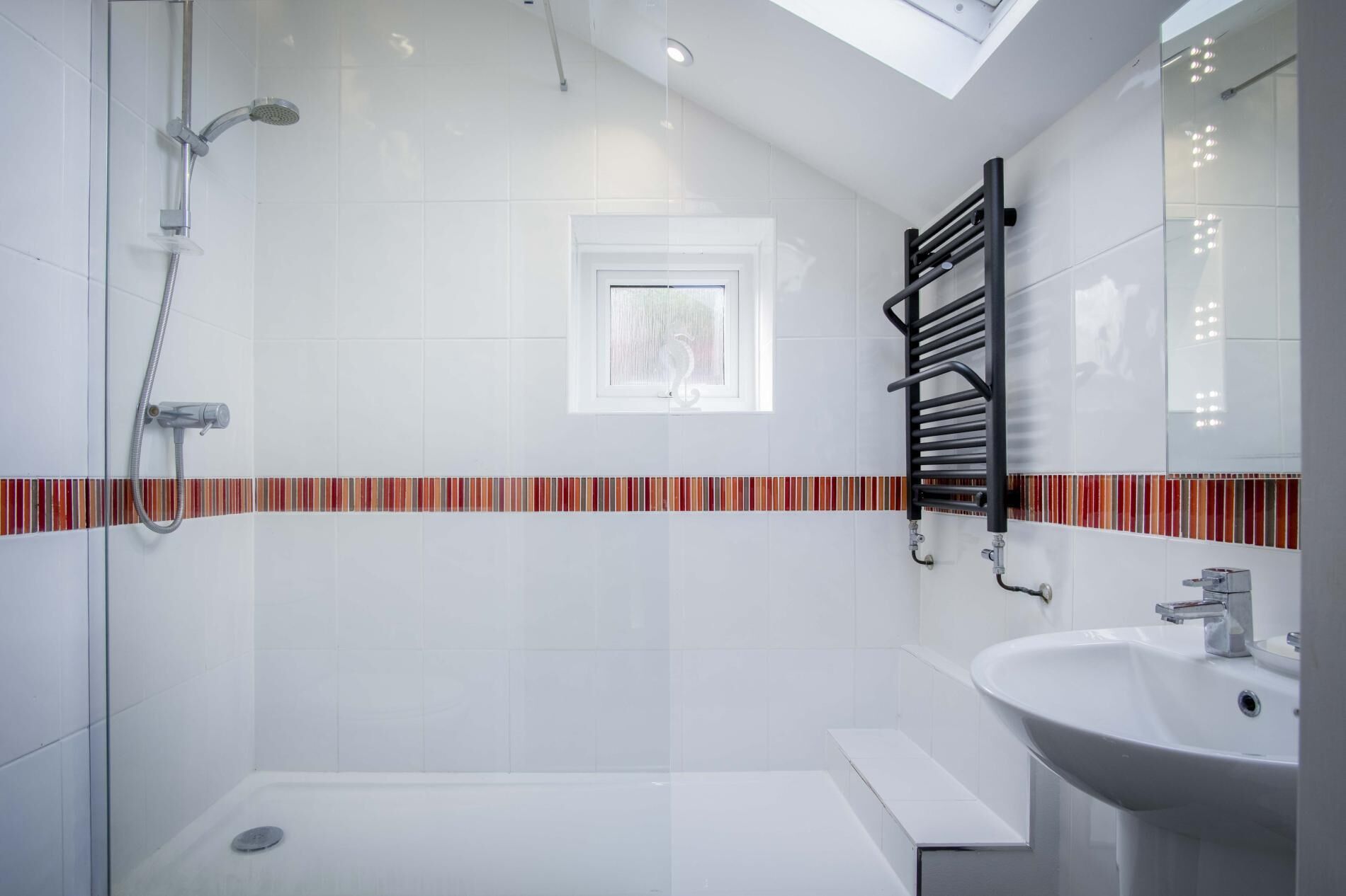 A modern bathroom with a glass shower enclosure, a white sink, and a black towel rack.