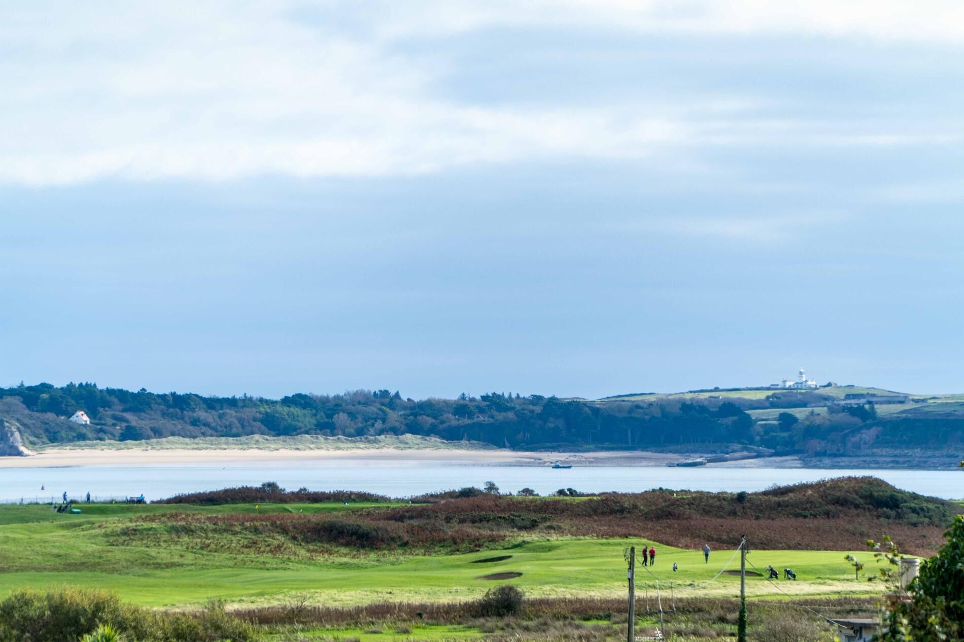Een kustlandschap met een golfbaan, een vuurtoren en een strand.