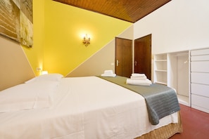 A hotel room with a bed, a nightstand, a wall-mounted light, a wardrobe, and a door.