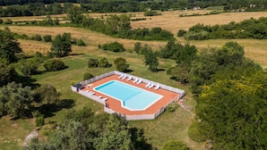 An aerial view of a rectangular swimming pool surrounded by a white fence, with lounge chairs and a small building nearby. - Room 'Santa Lorica - Camera 14' with Shared Pool, Shared Garden and Wi-Fi (Sassetta)