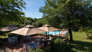 An outdoor patio area with tables and chairs, umbrellas, and a pool in the background. - Room 'Santa Lorica - Camera 14' with Shared Pool, Shared Garden and Wi-Fi (Sassetta)