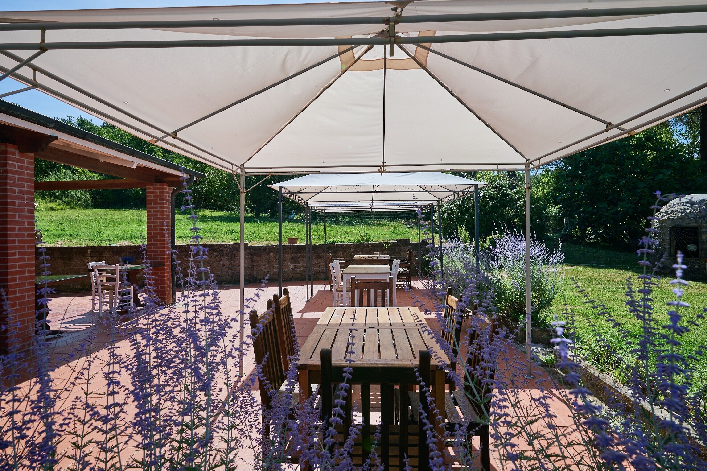 Een terras buiten met een overdekte zithoek, bakstenen muren en een tuin met paarse bloemen.