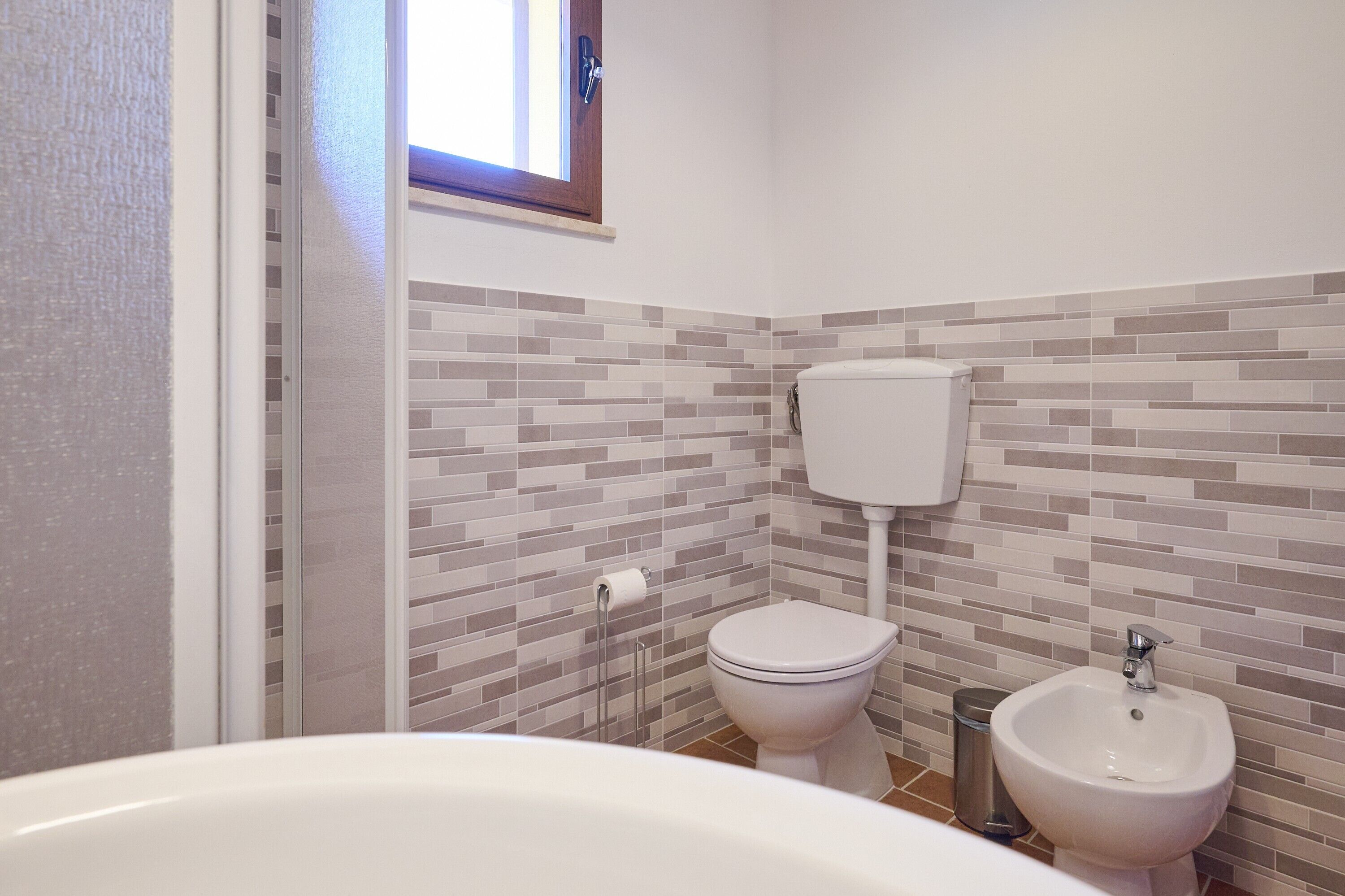 A bathroom with a toilet, bidet, and a window.