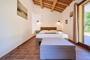 Un dormitorio con techo de madera, una cama con ropa blanca, un banco y vistas por una ventana.