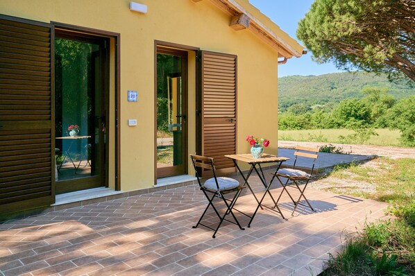 Un edificio con un patio, una mesa con sillas y vistas a un paisaje verde.