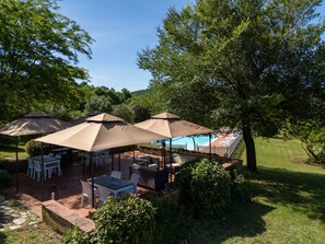 An outdoor patio area with tables and chairs, umbrellas, and a pool in the background.