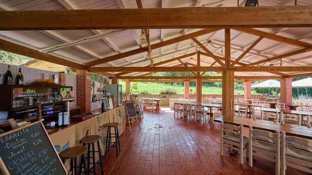 An outdoor café with wooden tables and chairs, a bar area with bottles and glasses, and a chalkboard menu. - Room 'Santa Lorica - Camera 20' with Shared Pool, Wi-Fi and Air Conditioning (Sassetta)