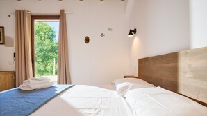 Ein Schlafzimmer mit Bett, Vorhängen, einer Wandlampe und Blick auf Grün.