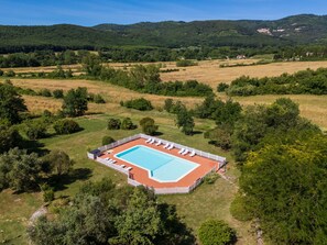 Une vue aérienne d’une piscine rectangulaire entourée d’une clôture blanche, avec des chaises longues et un petit bâtiment à proximité.