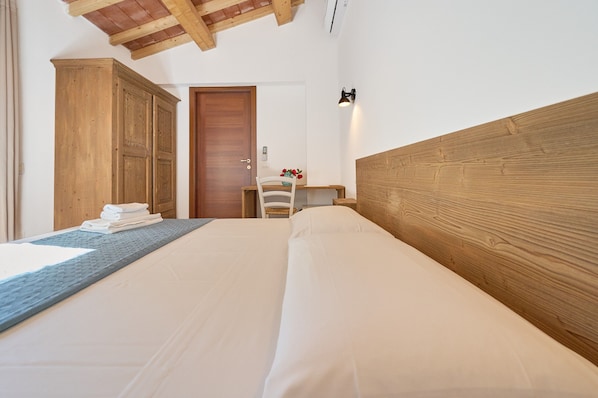 A bedroom with a bed, wooden headboard, a wardrobe, a desk with a chair, and a door.