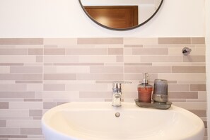 A bathroom with a white sink, a round mirror, and a tiled backsplash. - Room 'Santa Lorica - Camera 19' with Shared Pool, Wi-Fi and Air Conditioning (Sassetta)