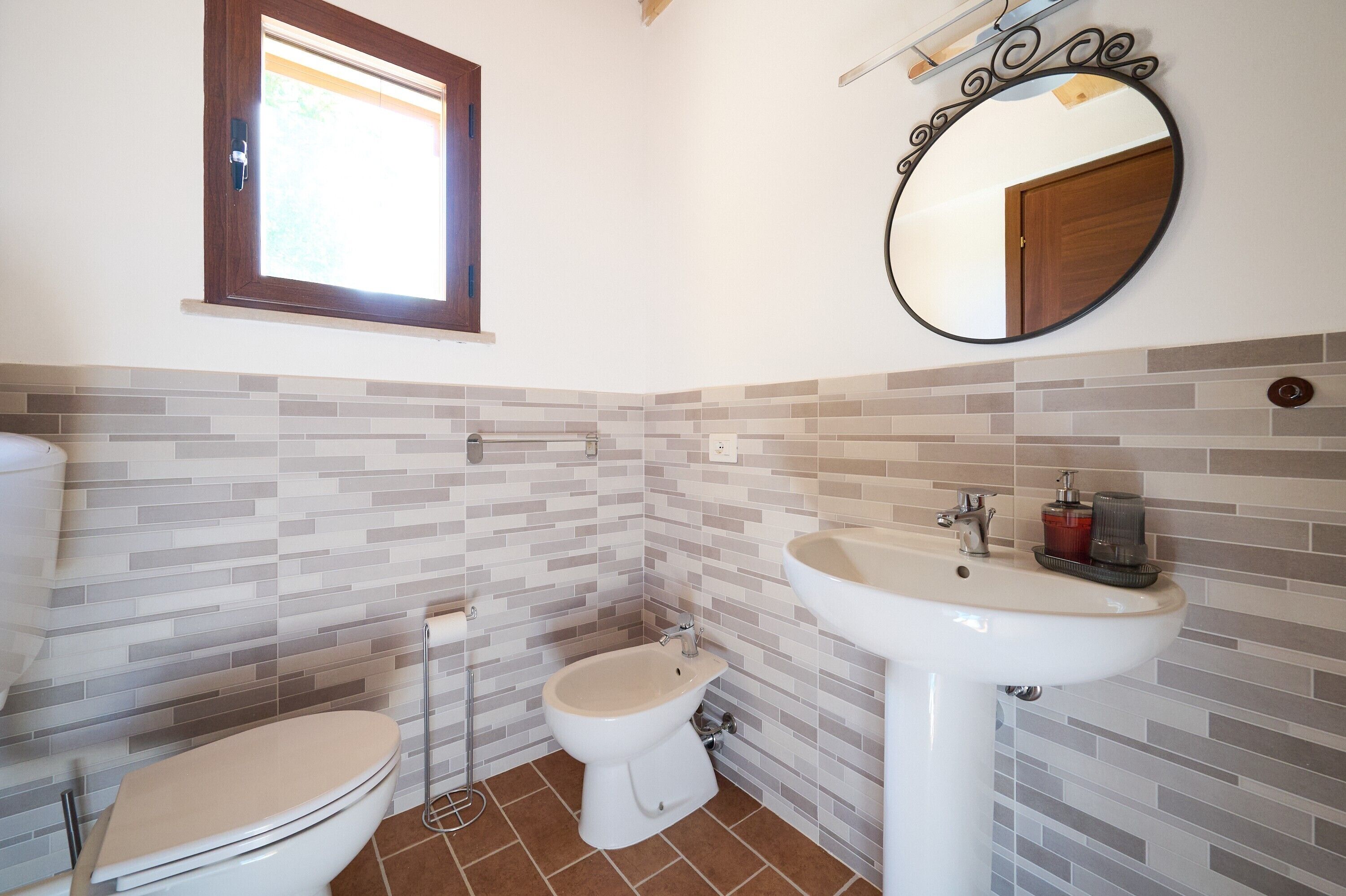 A bathroom with a toilet, bidet, and sink, tiled walls, and a window.