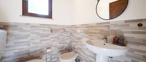 A bathroom with a toilet, bidet, and sink, tiled walls, and a window.