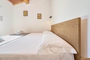 Un lit bien fait, avec du linge de lit blanc, une tête de lit en bois et deux tableaux encadrés accrochés au mur.