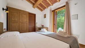 A bedroom with a large bed, wooden wardrobe, and a view of greenery through a window.