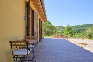 Un edificio con un patio empedrado, muebles de madera y vistas a un paisaje verde.