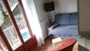 Una habitación acogedora con una mesa de comedor para dos, una silla roja, un sofá y vistas al exterior a través de una puerta.