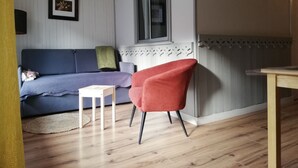 Una sala de estar con un sofá azul, un sillón rojo, una mesita blanca y una ventana con vistas.