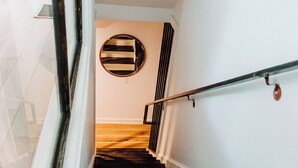 A wooden staircase with a metal handrail, white walls, and a circular mirror on the wall. - Discover Ponce Hideaway—an elegant 2BR, 2.5BA retreat in Midtown Atlanta. Modern-eclectic design, gold accents, and jewel tones set the scene. Enjoy a private patio, full kitchen, washer/dryer, & walkable access to Ponce City Market and Piedmont Park (Atlanta)