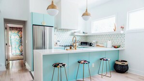 Une cuisine moderne dotée d’un grand îlot central, d’appareils électroménagers en acier inoxydable et de tabourets de bar aux couleurs vives.