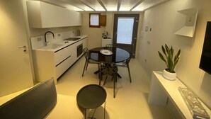 Een kleine keuken met witte kasten, een eettafel met stoelen, een kamerplant en een flatscreen televisie aan de muur.