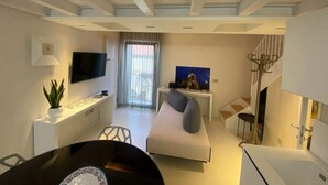 A modern living room with a sofa, a TV, a dining table, and a staircase. - Termoli - Casa Vacanza - BASTIONI QUATTRO (Termoli)