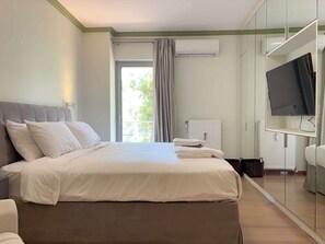 A hotel room with a bed, a television, a radiator, and a view of greenery outside. - Luxurious & Spacious Flat in Glyfada Center (Glifada)