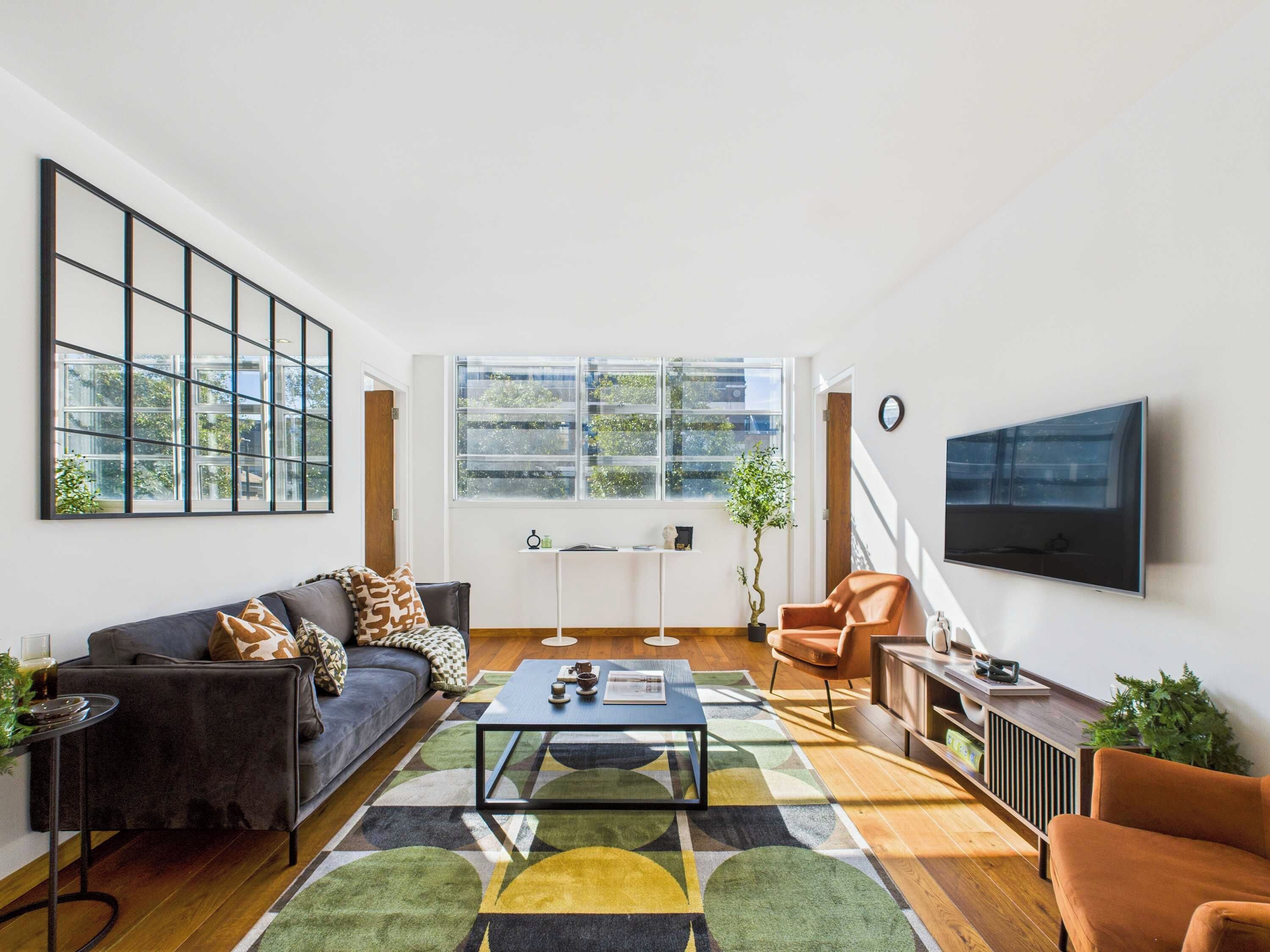 A modern living room with a sofa, armchair, coffee table, and a TV mounted on the wall.