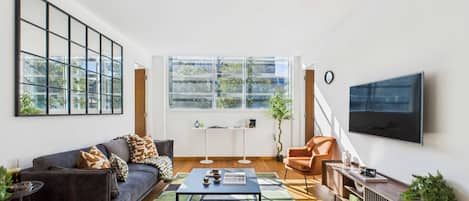 A modern living room with a sofa, armchair, coffee table, and a TV mounted on the wall.