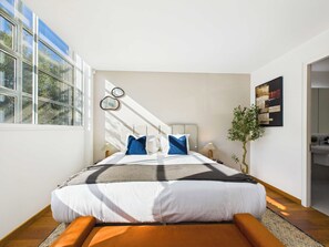 Une chambre moderne avec un grand lit, une vue sur l’extérieur par une fenêtre et une petite plante sur la table de chevet.