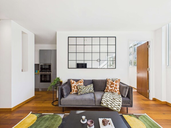 Un salon moderne avec un canapé gris, des coussins à motifs, une table basse avec des collations et une grande œuvre d’art abstraite accrochée au mur.