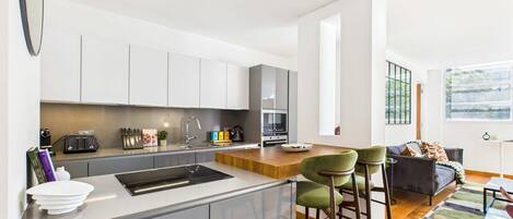 Una cocina moderna con una isla central, electrodomésticos integrados y una zona de comedor con taburetes de bar.