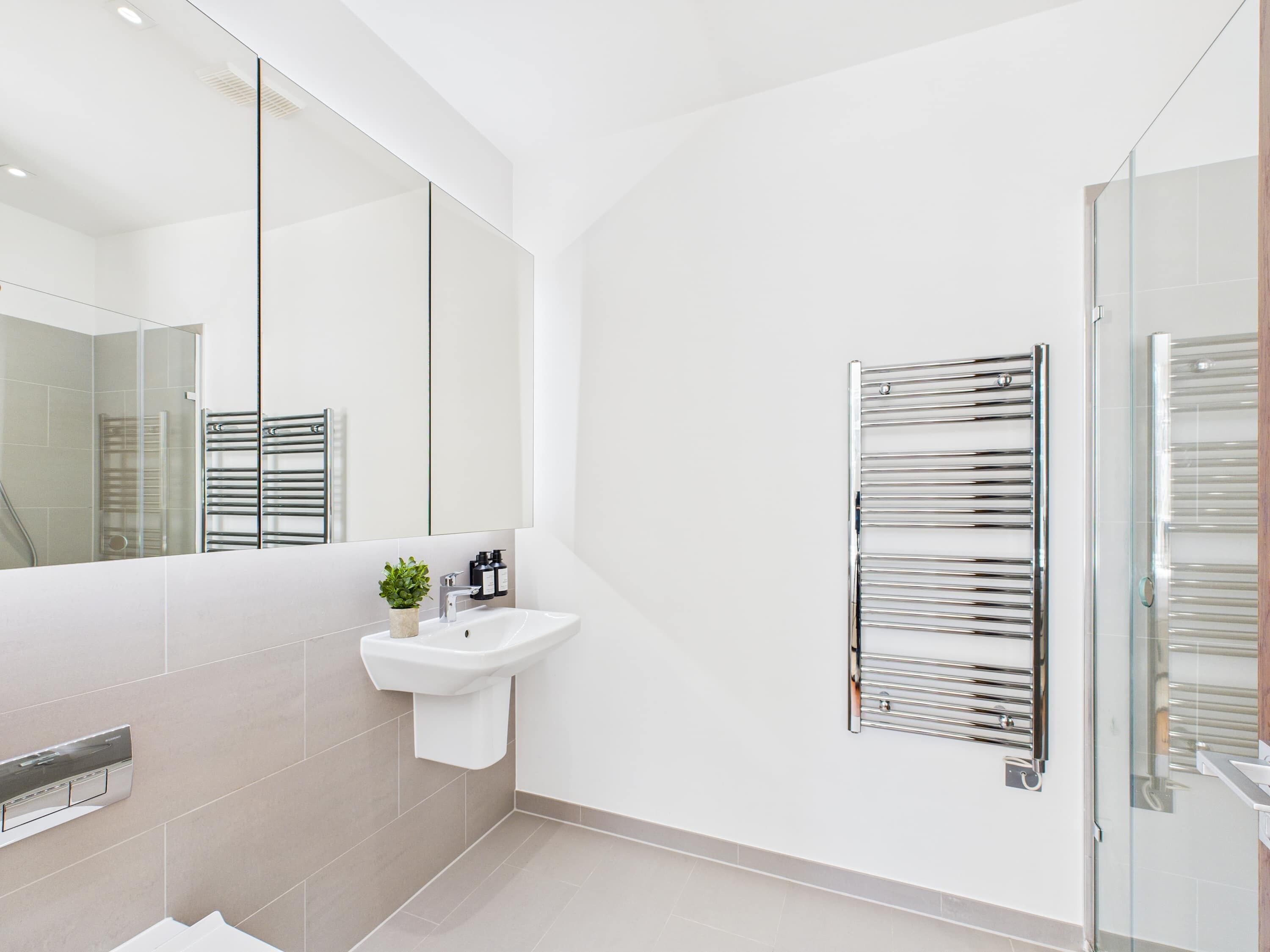 A modern bathroom with a large mirror, a sink, and a towel rack.