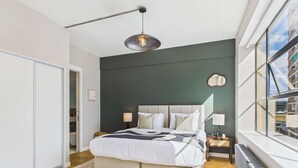 Une chambre moderne avec un grand lit, un luminaire suspendu et une vue sur la ville grâce à de grandes fenêtres.