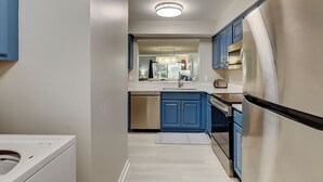 A modern kitchen with blue cabinets, a stainless steel refrigerator, and a built-in oven. - Courtside 52- ground level 2BR flat! (Hilton Head Island)