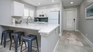 Une cuisine moderne avec des meubles blancs, un îlot central doté de tabourets, un four à micro-ondes et un réfrigérateur.