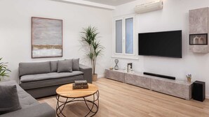 Un salon moderne avec un canapé gris, une table basse en bois, un grand téléviseur à écran plat fixé au mur et une plante en pot.