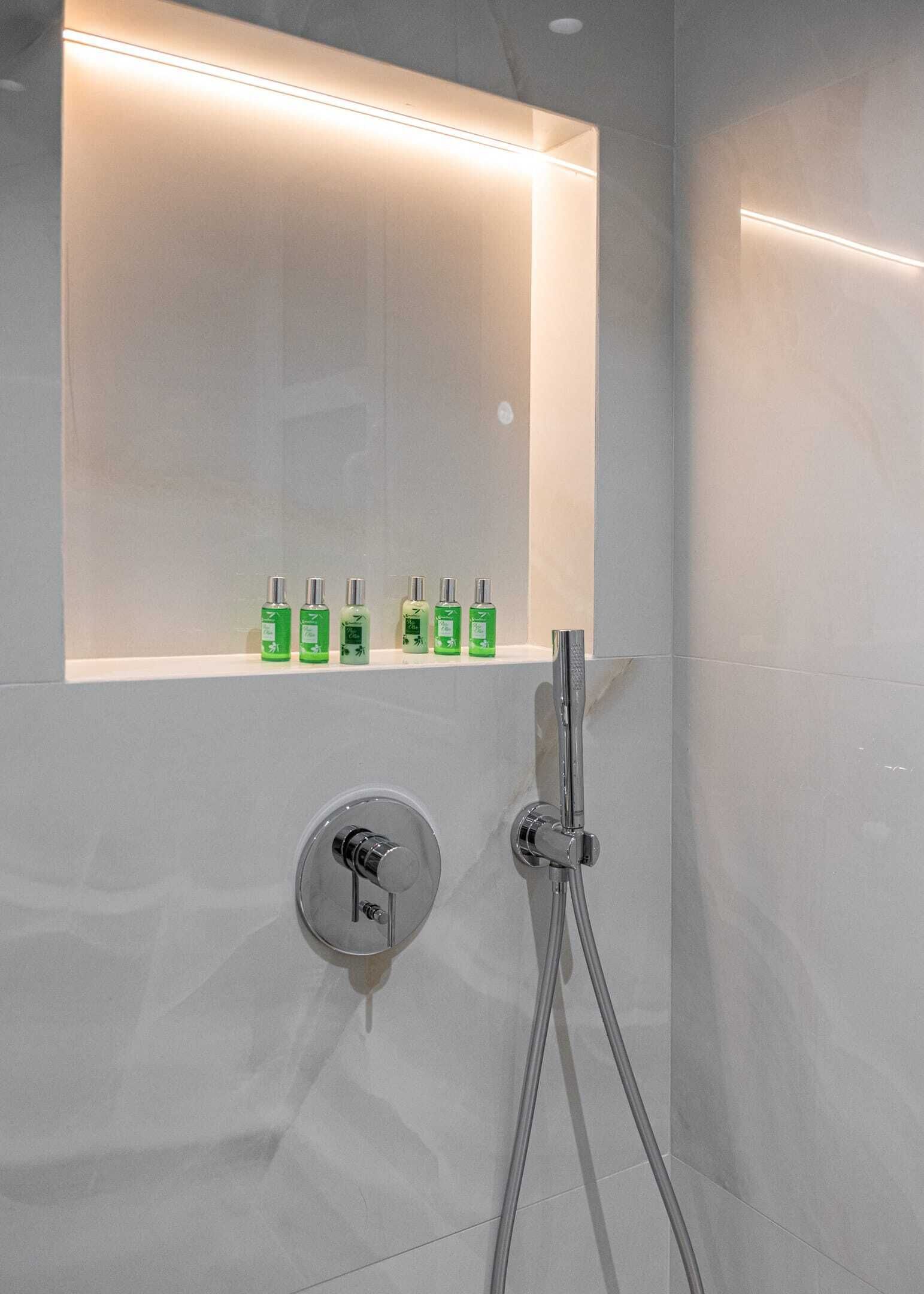 Ein Badezimmer mit Dusche, Spiegel und Ablage mit grünen Flaschen.