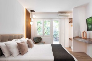 A modern bedroom with a bed, a chair, a TV, and a window with a view of greenery. - Acropolis Holmes Residence, Apartment (Athens)