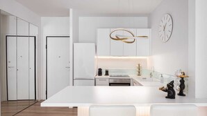 Une cuisine moderne dotée d’un îlot central, de meubles blancs et d’un four encastré. Deux horloges sont accrochées au mur et une sculpture décorative est posée sur l’îlot.