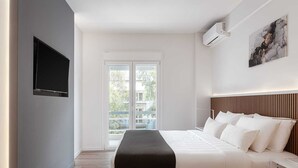 Une chambre moderne dotée d’un grand lit, d’un téléviseur à écran plat et d’un balcon offrant une vue sur la verdure.