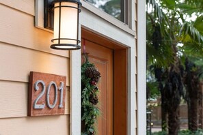 Un numéro de maison, le « 201 », fixé sur une planche de bois, une porte ornée d’une guirlande et un luminaire fixé au mur.