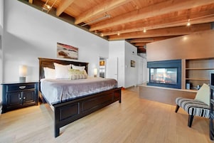 Un dormitorio con una cama grande, cabecera de madera, mesitas de noche, una silla y una chimenea.