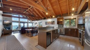 A spacious kitchen with a large island, wooden ceiling beams, and a view of the outdoors. - Mariner's Loft (Salt Spring Island)