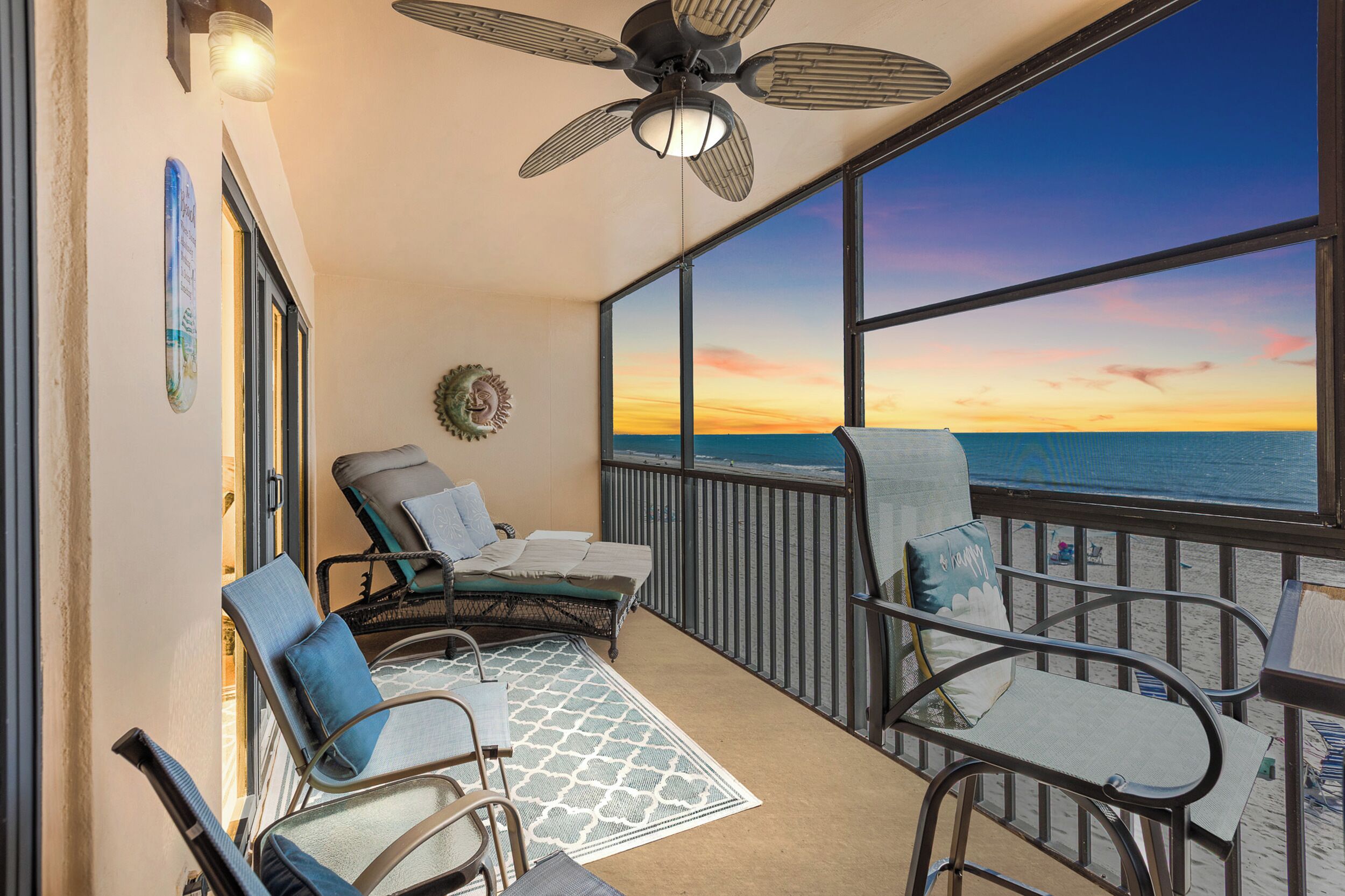 A balcony with a view of the ocean at sunset, furnished with chairs and a table.