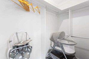 Una stanza con una parete bianca, un’altalena per bambini grigia e un marsupio con motivo camouflage appeso a un portariviste metallico.